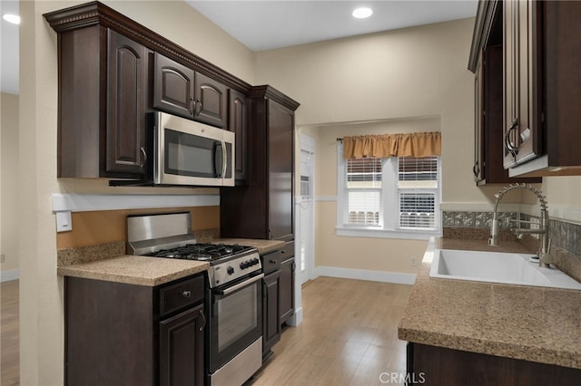 kitchen featuring dark brown cabinets, sink, light wood-type flooring, and stainless steel appliances