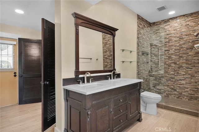 bathroom with hardwood / wood-style floors, vanity, toilet, and tiled shower