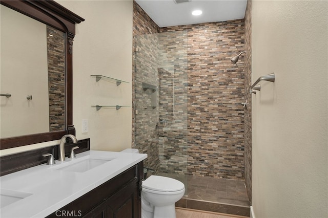 bathroom featuring a tile shower, hardwood / wood-style floors, vanity, and toilet