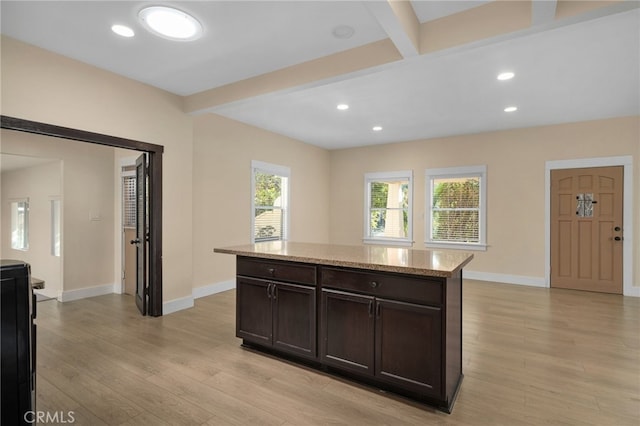 kitchen featuring beam ceiling, dark brown cabinetry, light stone countertops, a center island, and light hardwood / wood-style flooring