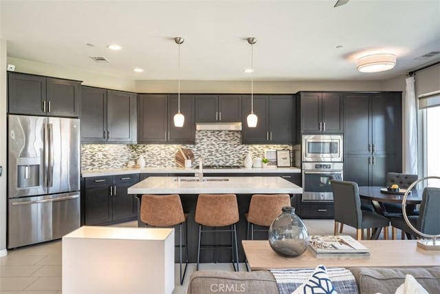 kitchen with pendant lighting, decorative backsplash, light tile patterned floors, an island with sink, and stainless steel appliances