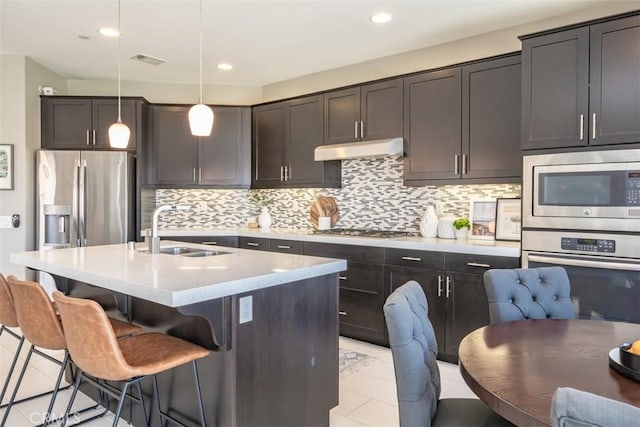 kitchen featuring backsplash, sink, an island with sink, appliances with stainless steel finishes, and decorative light fixtures