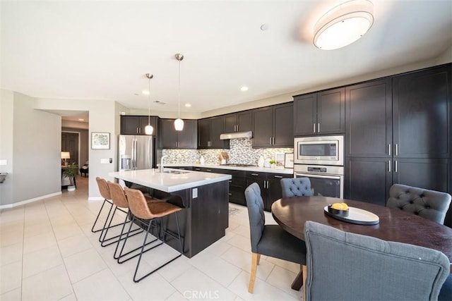 kitchen featuring a kitchen breakfast bar, sink, an island with sink, appliances with stainless steel finishes, and decorative light fixtures