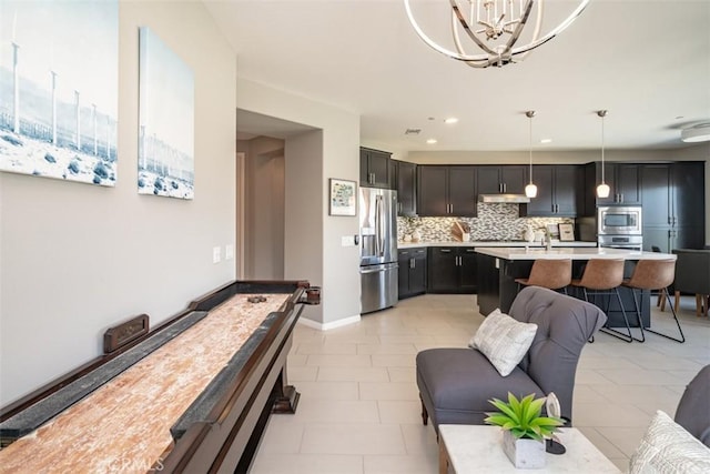 interior space with pendant lighting, decorative backsplash, an island with sink, appliances with stainless steel finishes, and a notable chandelier