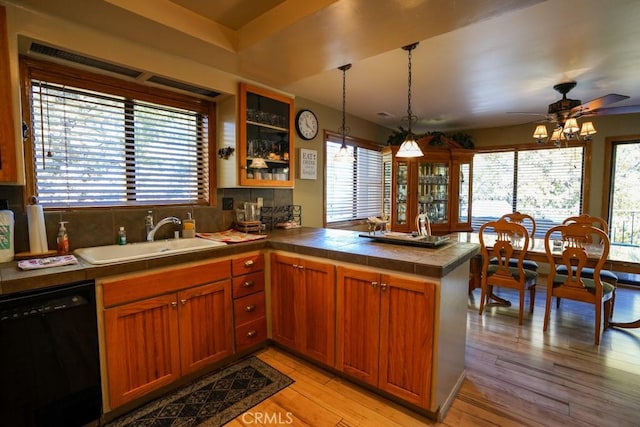 kitchen featuring kitchen peninsula, sink, black dishwasher, light hardwood / wood-style floors, and hanging light fixtures