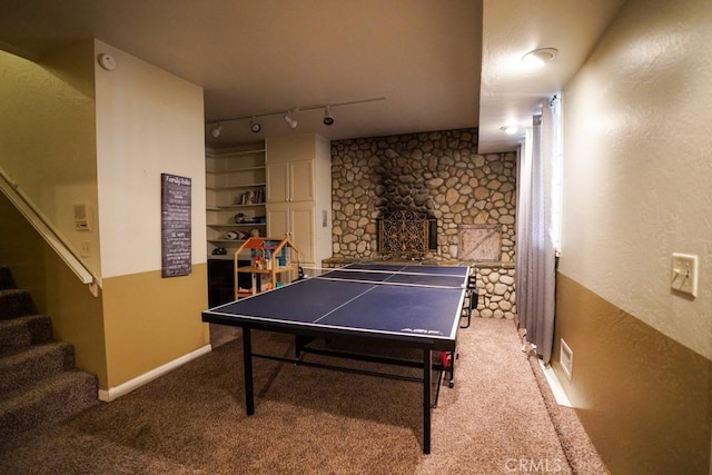 game room with carpet flooring, rail lighting, and a stone fireplace