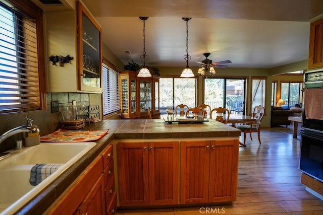 kitchen featuring light wood-type flooring, backsplash, ceiling fan, sink, and hanging light fixtures