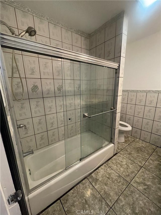 bathroom featuring tile patterned floors, combined bath / shower with glass door, tile walls, and toilet