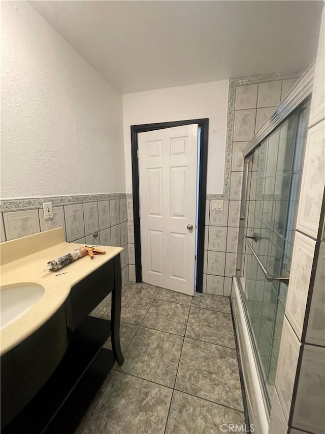 bathroom with tile patterned floors, a tile shower, vanity, and tile walls