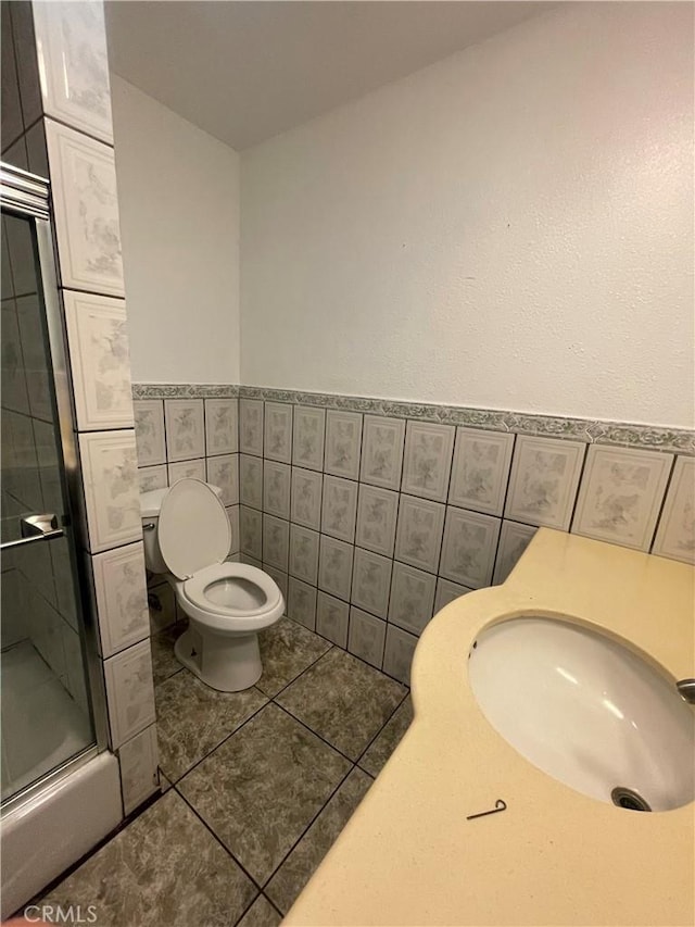 bathroom featuring sink, tile patterned floors, an enclosed shower, toilet, and tile walls