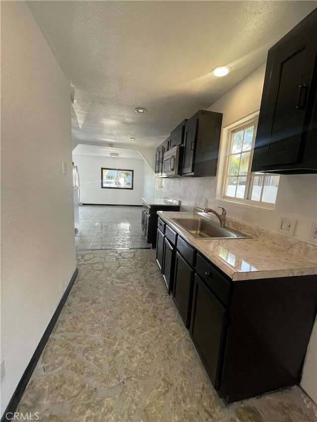 kitchen featuring a textured ceiling, stainless steel appliances, vaulted ceiling, and sink