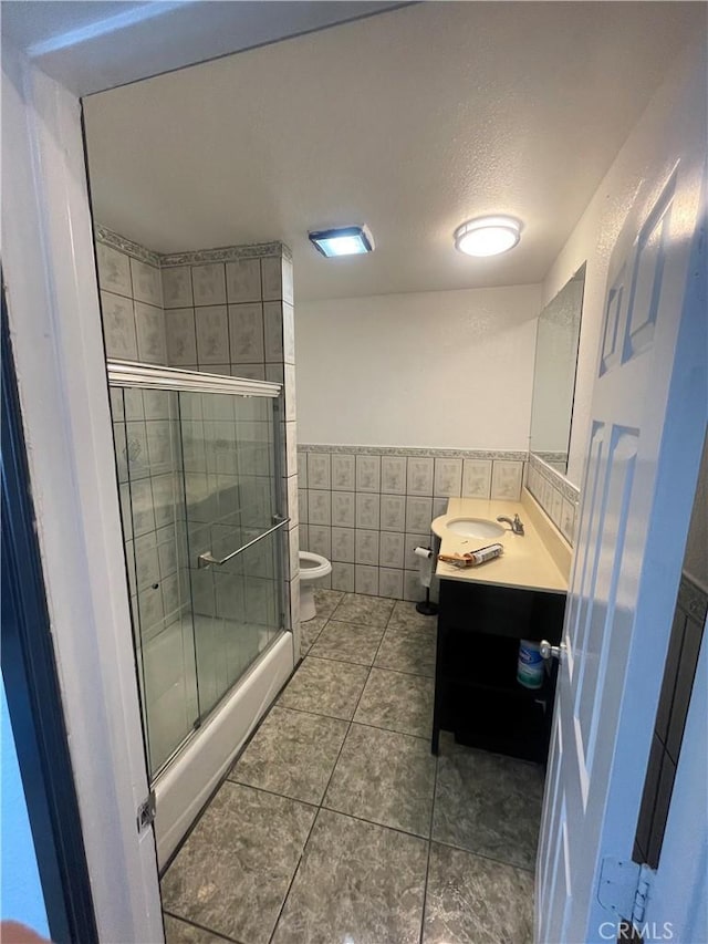 bathroom with tile patterned floors, an enclosed shower, vanity, tile walls, and toilet