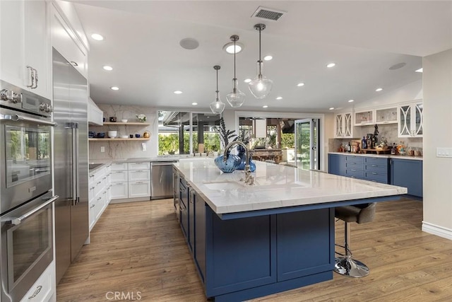 kitchen with decorative backsplash, appliances with stainless steel finishes, light wood-type flooring, a spacious island, and white cabinetry