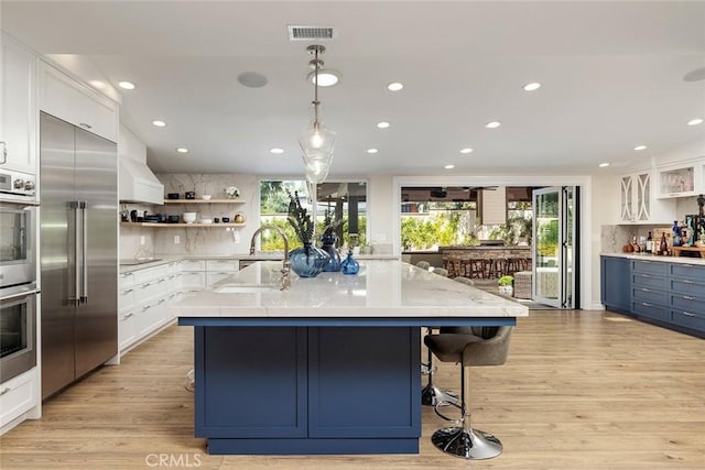 kitchen with white cabinets, a large island, light wood-type flooring, and stainless steel appliances