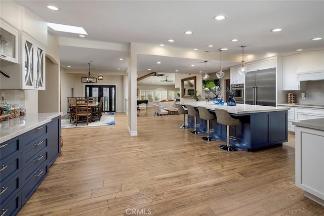 kitchen with a kitchen bar, light wood-type flooring, pendant lighting, stainless steel built in fridge, and white cabinets