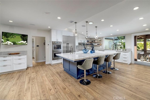 kitchen featuring a kitchen island with sink, appliances with stainless steel finishes, light hardwood / wood-style floors, light stone counters, and white cabinetry