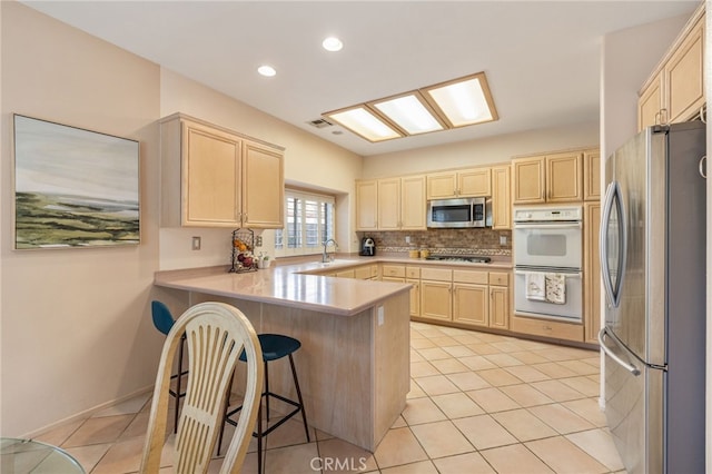 kitchen featuring kitchen peninsula, a breakfast bar, stainless steel appliances, light brown cabinets, and light tile patterned flooring