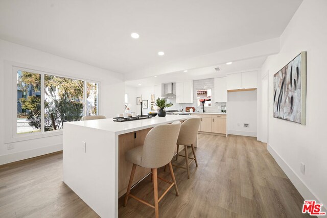 kitchen with white cabinetry, wall chimney exhaust hood, tasteful backsplash, light hardwood / wood-style floors, and a kitchen island