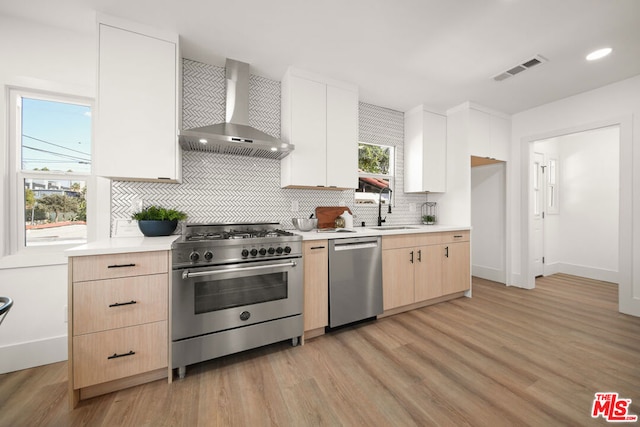 kitchen featuring light wood-type flooring, backsplash, wall chimney exhaust hood, stainless steel appliances, and sink