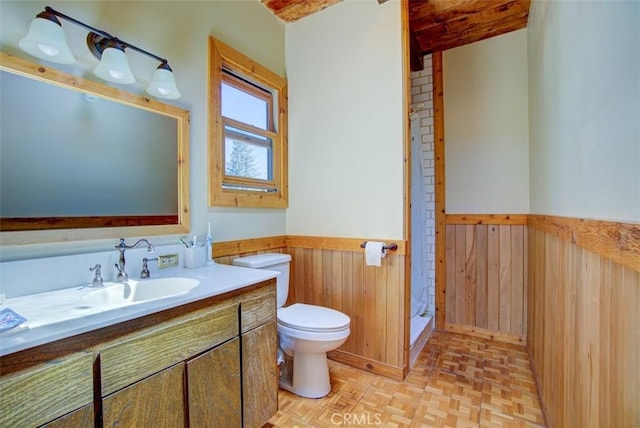 bathroom featuring parquet flooring, vanity, beam ceiling, toilet, and wood walls