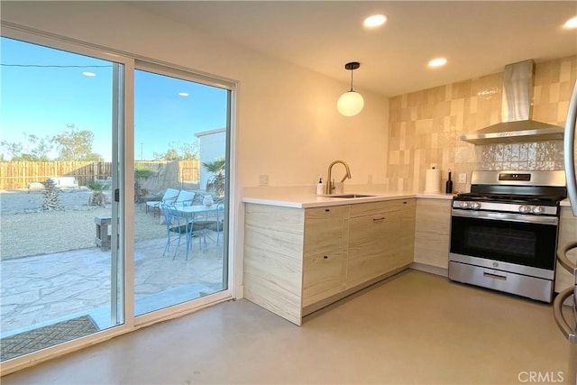 kitchen with wall chimney range hood, sink, stainless steel stove, tasteful backsplash, and decorative light fixtures