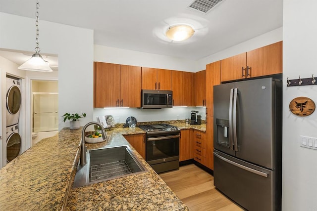 kitchen featuring sink, hanging light fixtures, light wood-type flooring, stacked washer / drying machine, and stainless steel appliances