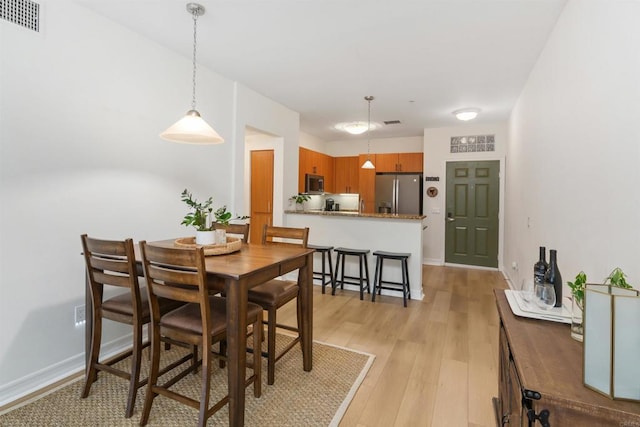 dining room with light wood finished floors, baseboards, and visible vents