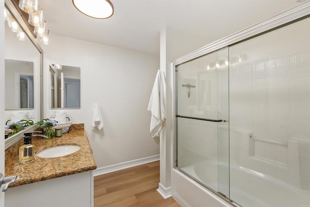 full bath featuring enclosed tub / shower combo, wood finished floors, a sink, baseboards, and double vanity