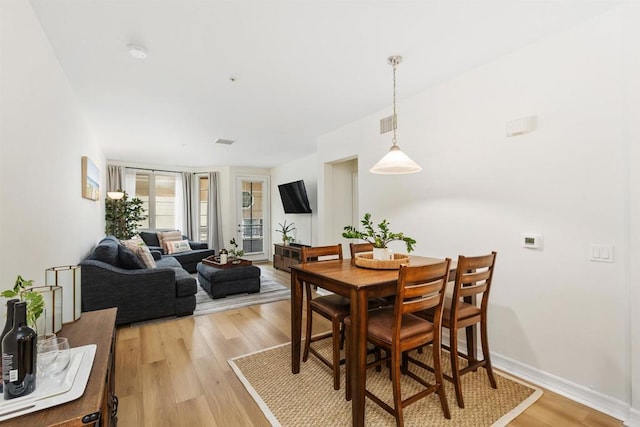 dining room with light wood-type flooring, visible vents, and baseboards