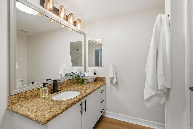 bathroom featuring visible vents, vanity, wood finished floors, baseboards, and walk in shower