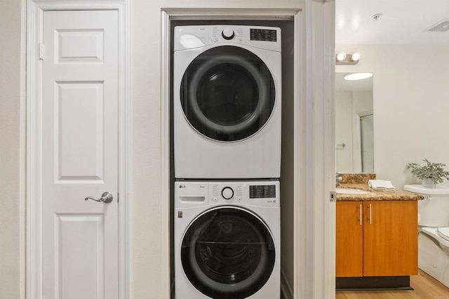 clothes washing area with light wood finished floors, a sink, visible vents, and stacked washer / drying machine