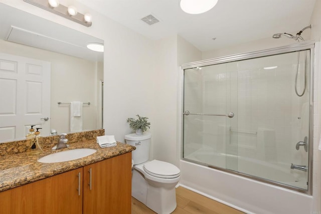 bathroom featuring visible vents, toilet, combined bath / shower with glass door, vanity, and wood finished floors