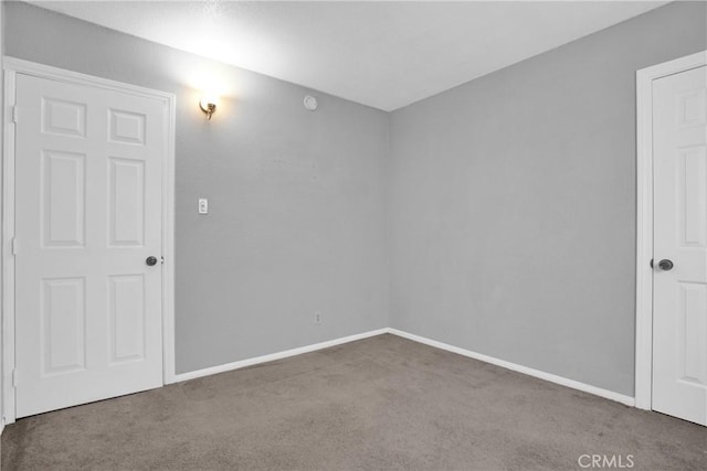 spare room featuring dark colored carpet and baseboards