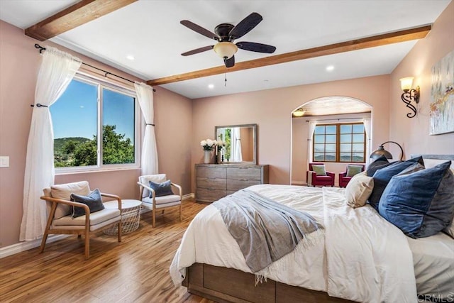 bedroom with beam ceiling, light wood-type flooring, multiple windows, and ceiling fan