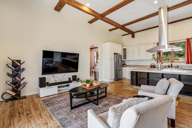 living room featuring beamed ceiling, a towering ceiling, and light hardwood / wood-style flooring