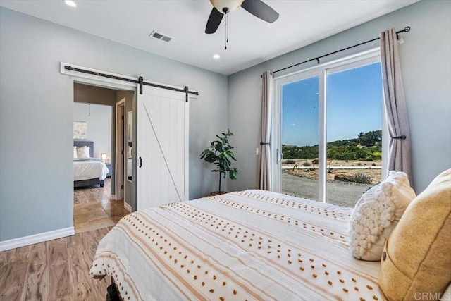 bedroom with ceiling fan, a barn door, access to exterior, and light hardwood / wood-style floors