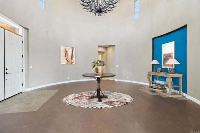 entrance foyer with concrete flooring, baseboards, a high ceiling, and an inviting chandelier