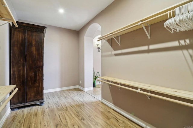 walk in closet with arched walkways and light wood-style floors