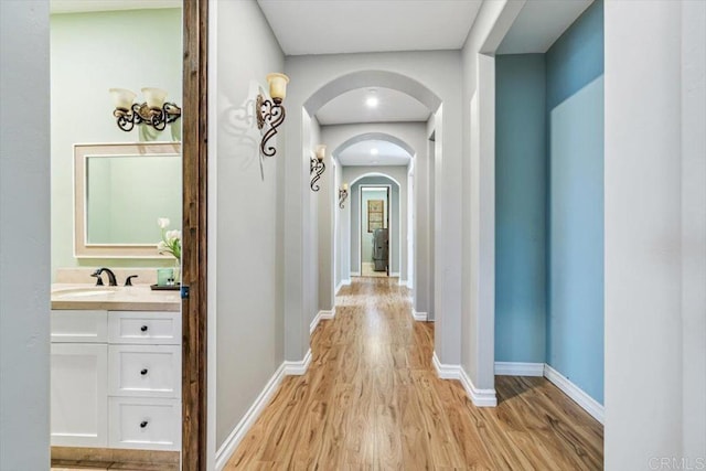 hallway with arched walkways, light wood finished floors, a sink, and baseboards