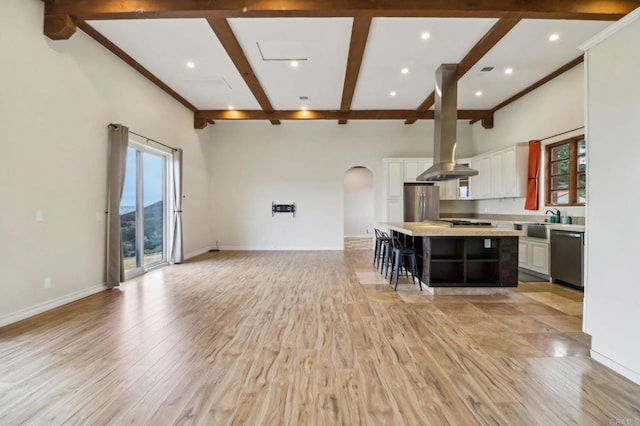 kitchen with arched walkways, beamed ceiling, island exhaust hood, stainless steel appliances, and light countertops