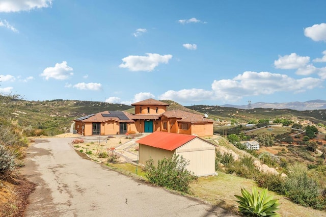 mediterranean / spanish home featuring roof mounted solar panels, a mountain view, fence, and an outbuilding