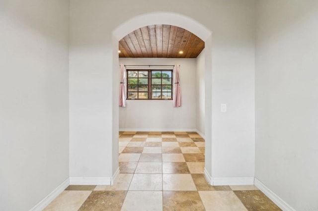 unfurnished room featuring arched walkways, wood ceiling, and baseboards