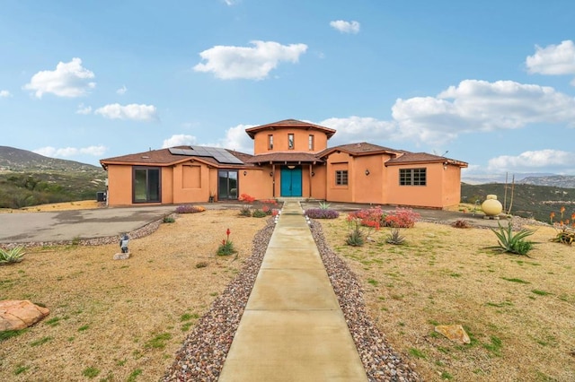 mediterranean / spanish-style house featuring fence, roof mounted solar panels, a mountain view, a front lawn, and stucco siding