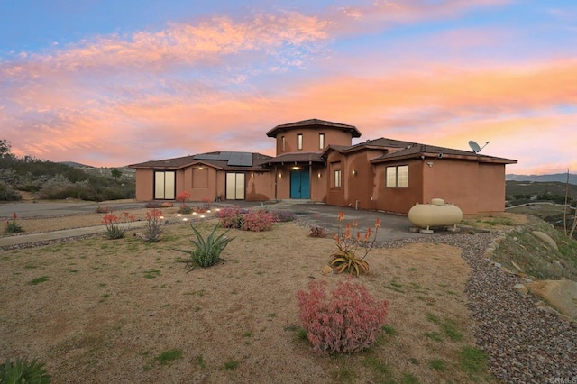 view of front of house with driveway, a patio, and roof mounted solar panels