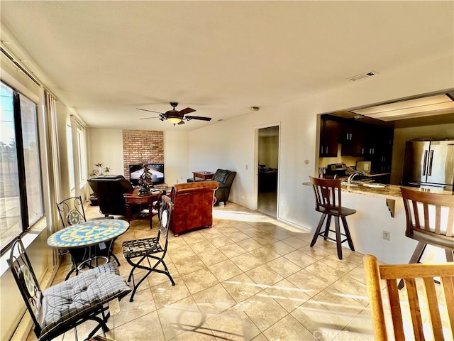 dining space with ceiling fan, a fireplace, and light tile patterned flooring