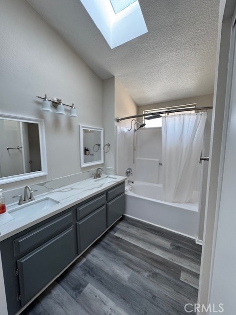 bathroom featuring lofted ceiling with skylight, a textured ceiling, vanity, shower / bathtub combination with curtain, and hardwood / wood-style floors