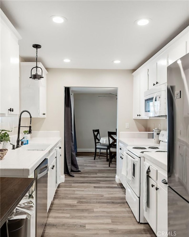 kitchen with white cabinetry, sink, light hardwood / wood-style flooring, decorative light fixtures, and appliances with stainless steel finishes