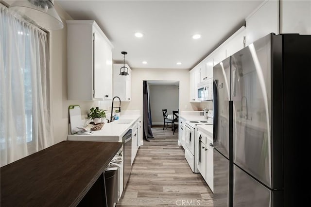 kitchen featuring sink, appliances with stainless steel finishes, decorative light fixtures, light hardwood / wood-style floors, and white cabinetry