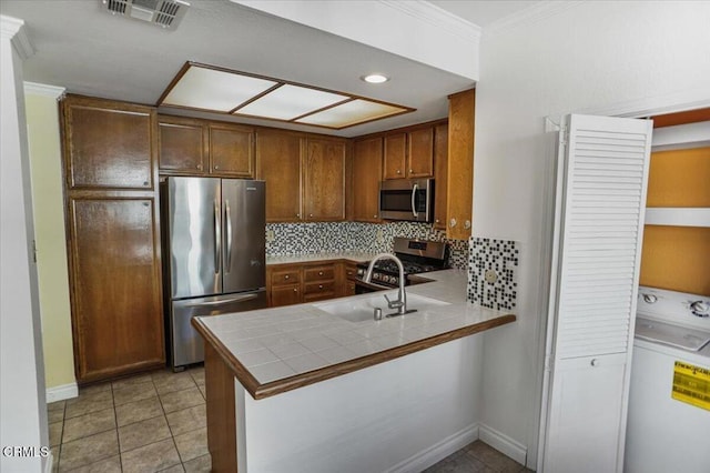 kitchen featuring kitchen peninsula, appliances with stainless steel finishes, tasteful backsplash, washer / clothes dryer, and tile counters