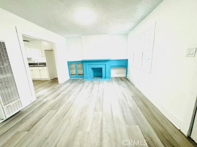 unfurnished living room featuring a textured ceiling, light wood-type flooring, and sink